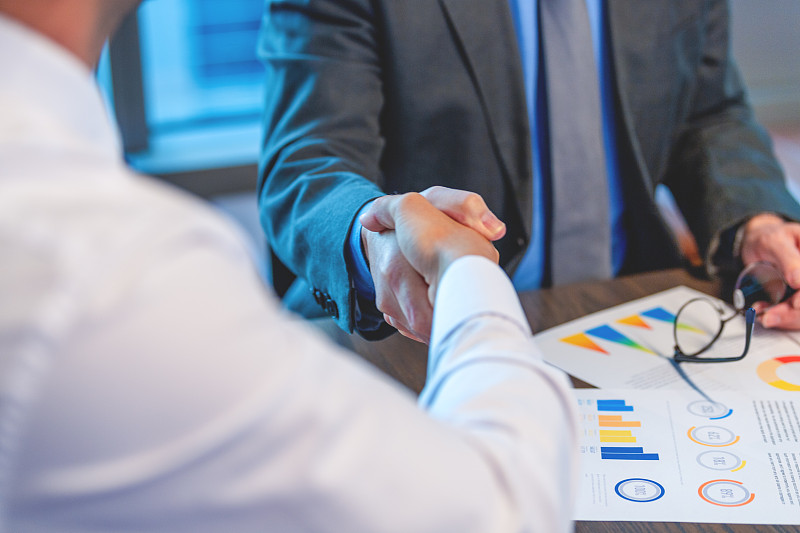 商人们握手的特写。两人都穿着职业装，有文件和一台电脑图片下载